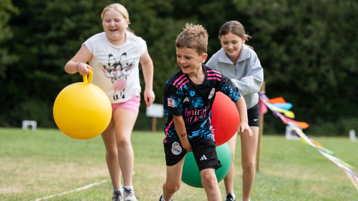 Three children play a running race holding space hoppers.